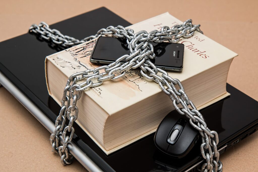 phone, book, laptop and computer mouse wrapped in chains